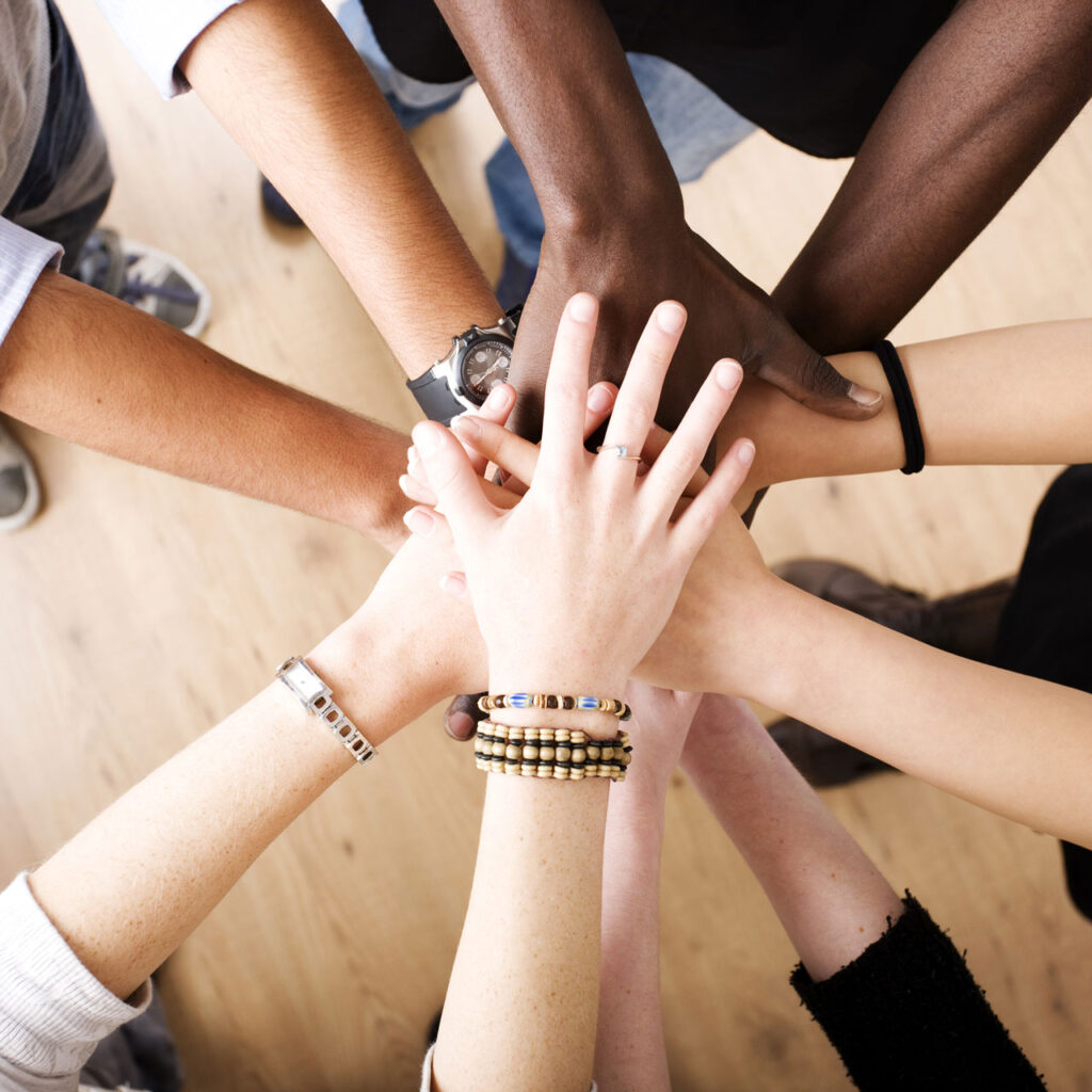 Changitors_Start_Top_Team Verschiedenfarbige Hände mehrerer Menschen liegen übereinander und symbolisieren Teamwork und Zusammenhalt